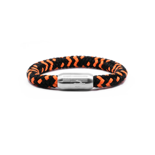 “Geflochtenes Armband in Schwarz und Orange mit einem Edelstahl-Magnetverschluss, verziert durch ein eingraviertes Dreizack-Symbol. Modernes und kraftvolles Design, inspiriert von Dynamik und Stärke.”
