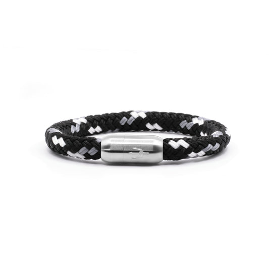 “Geflochtenes Armband in Schwarz-Weiß mit einem Edelstahl-Magnetverschluss, verziert durch eine eingravierte Dreizack-Symbolik. Modernes und minimalistisches Design, inspiriert von Wellen und Kontrasten.”