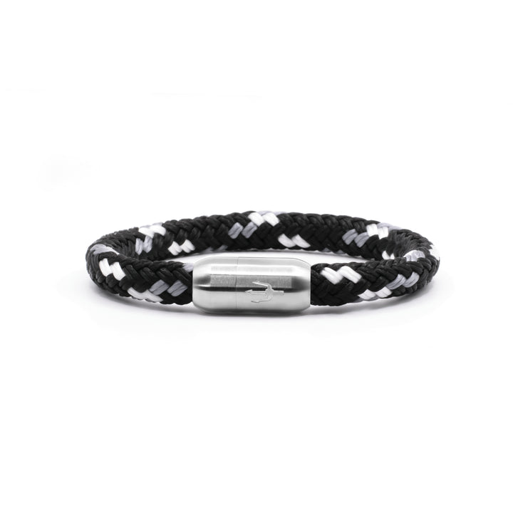 “Geflochtenes Armband in Schwarz-Weiß mit einem Edelstahl-Magnetverschluss, verziert durch eine eingravierte Dreizack-Symbolik. Modernes und minimalistisches Design, inspiriert von Wellen und Kontrasten.”