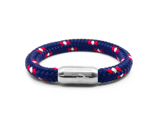 “Geflochtenes Armband in Marineblau mit roten und weißen Akzenten, kombiniert mit einem Edelstahl-Magnetverschluss, verziert durch ein eingraviertes Dreizack-Symbol. Maritimes und sportliches Design für einen klassischen Look.”