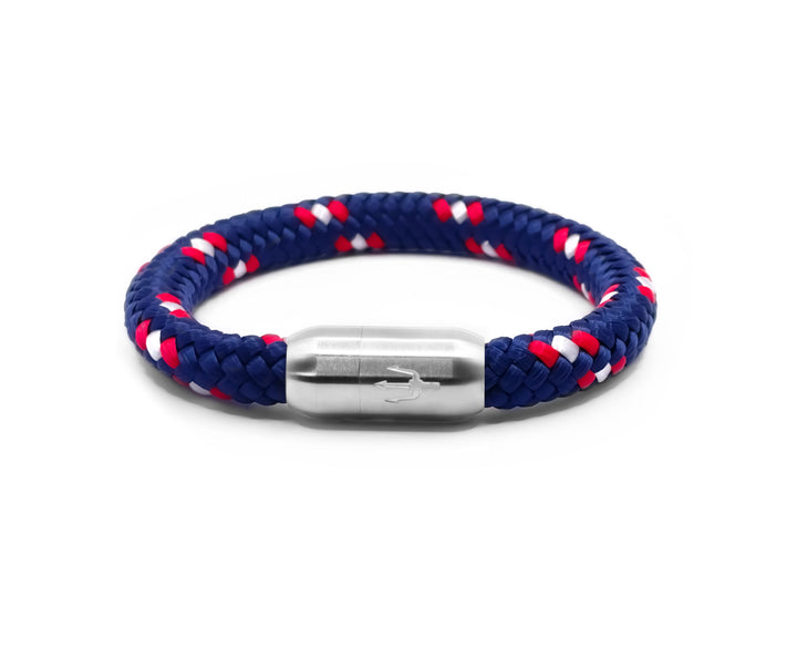 “Geflochtenes Armband in Marineblau mit roten und weißen Akzenten, kombiniert mit einem Edelstahl-Magnetverschluss, verziert durch ein eingraviertes Dreizack-Symbol. Maritimes und sportliches Design für einen klassischen Look.”