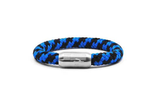 “Geflochtenes Armband in Blau und Schwarz mit einem Edelstahl-Magnetverschluss, verziert durch ein eingraviertes Dreizack-Symbol. Kraftvolles maritimes Design, das Tiefe und Dynamik vereint.”