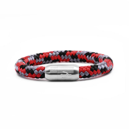 “Geflochtenes Armband in Rot, Schwarz und Grau mit einem Edelstahl-Magnetverschluss, verziert durch ein eingraviertes Dreizack-Symbol. Kraftvolles und dynamisches Design, inspiriert von der Energie eines Vulkans.”