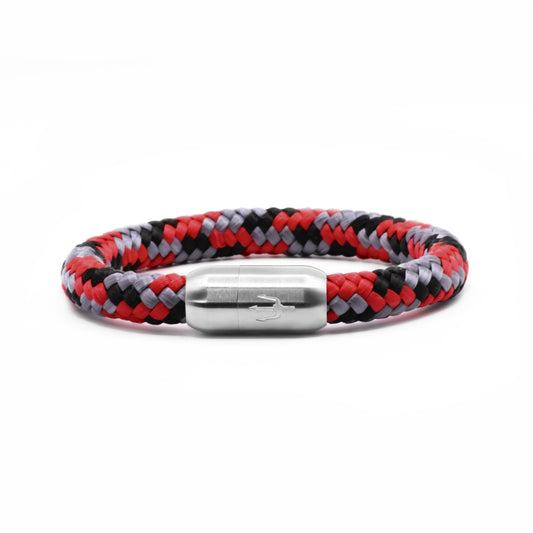 “Geflochtenes Armband in Rot, Schwarz und Grau mit einem Edelstahl-Magnetverschluss, verziert durch ein eingraviertes Dreizack-Symbol. Kraftvolles und dynamisches Design, inspiriert von der Energie eines Vulkans.”