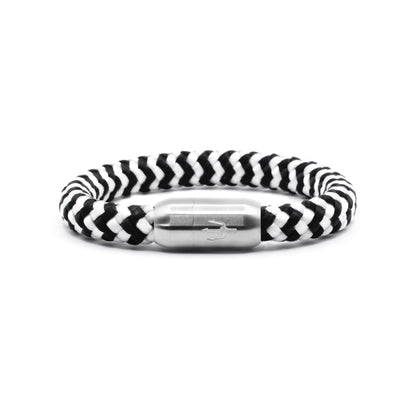 “Geflochtenes Armband in Schwarz-Weiß mit einem Edelstahl-Magnetverschluss, verziert durch eine eingravierte Dreizack-Symbolik. Markantes und elegantes Design, inspiriert von natürlichen Kontrasten.”