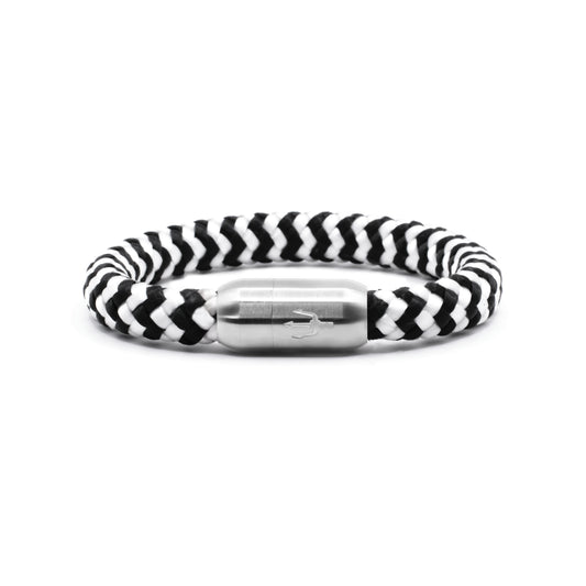 “Geflochtenes Armband in Schwarz-Weiß mit einem Edelstahl-Magnetverschluss, verziert durch eine eingravierte Dreizack-Symbolik. Markantes und elegantes Design, inspiriert von natürlichen Kontrasten.”