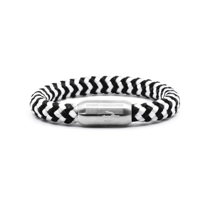 “Geflochtenes Armband in Schwarz-Weiß mit einem Edelstahl-Magnetverschluss, verziert durch eine eingravierte Dreizack-Symbolik. Markantes und elegantes Design, inspiriert von natürlichen Kontrasten.”